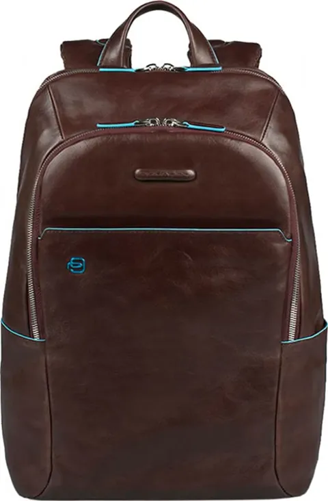 The backpack stands face-on against white: dark brown leather with a sheen, turquoise piping along the zips, a patch poc