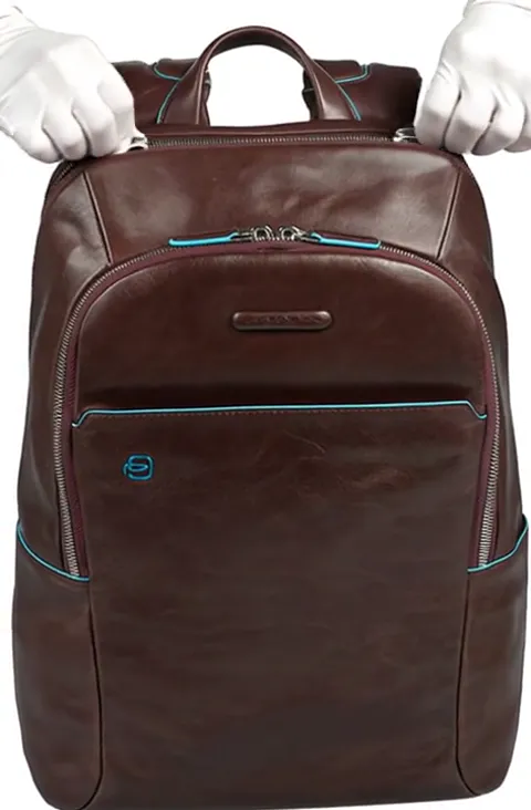 White-gloved hands take the top handle. The leather does not crease under pressure — the body holds its shape on a rigid