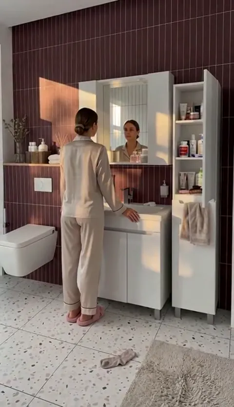 The window light turns warm and the mirror catches her face. The mirror cabinet proves to open on a hinge rather than be