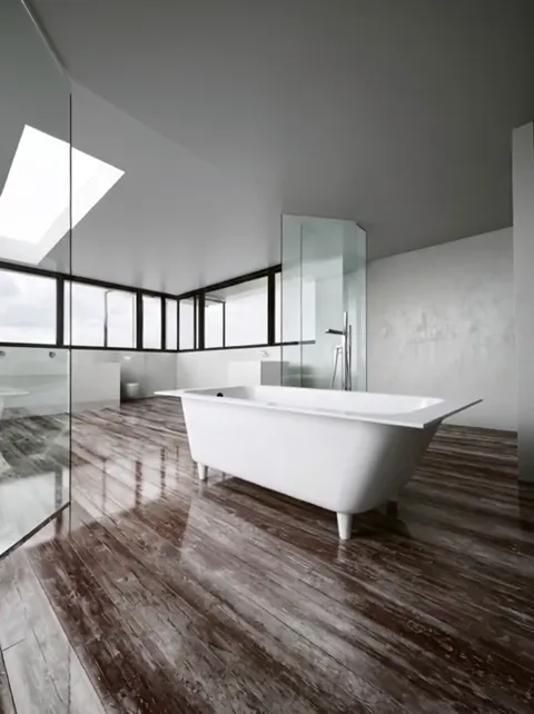 A bright attic bathroom: a freestanding bath on low feet by a full-height window, a wooden floor, a glass shower screen.