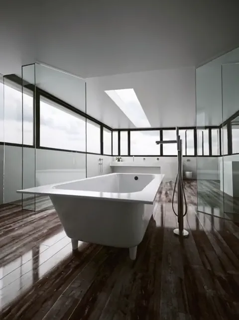 The arc continues and a floor-mounted tap enters. The distance from bath to wall becomes clear — it stands free rather t