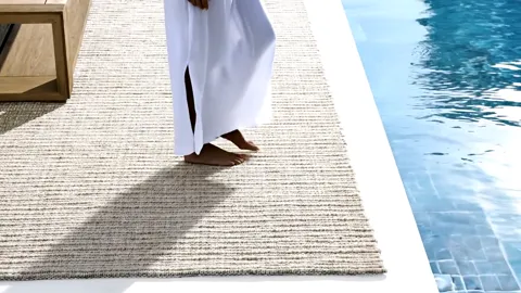 A woman in white walks across it. A bare foot on the weave — the surface is dense and does not slip on stone.