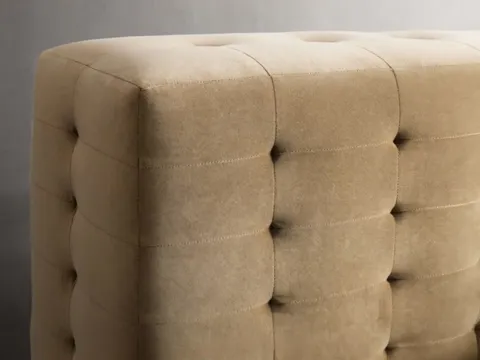 Macro on the corner of the headboard: beige fabric in deep buttoning, every square drawn in by hand. The volume of the f
