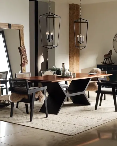 A dining room: a long walnut table on a black geometric base, black chairs with woven backs, two lantern pendants above,