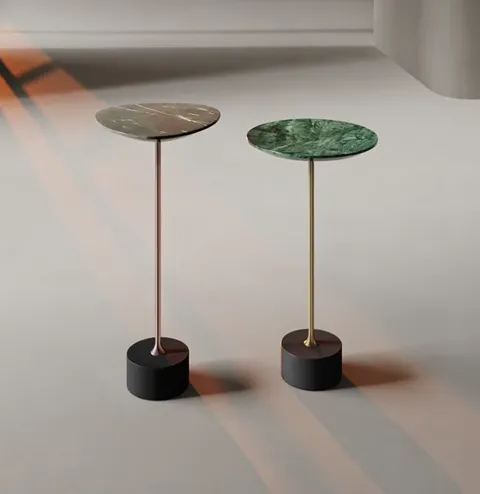 Two round side tables on slim stems with black bases stand in an empty, bright room. The tops differ: one dark veined st