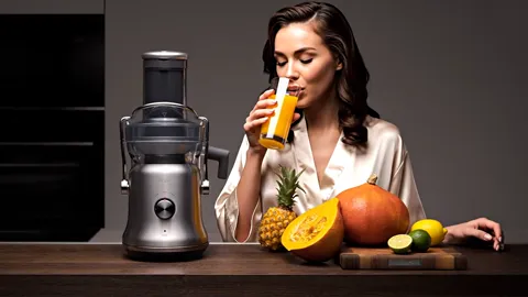 A woman takes the glass. The height of the machine against a person reads, and the chute is wide — a whole apple goes in