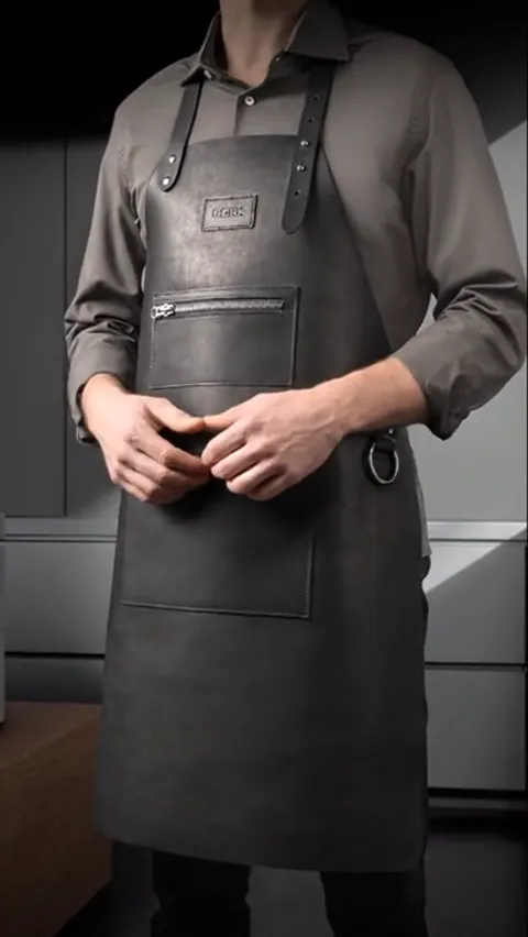He straightens the apron. The leather is soft: it follows the body rather than standing like armour — impossible to tell