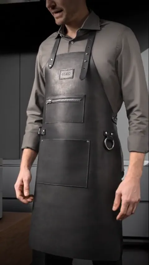 A wider frame shows the apron to the hem. A side ring for a towel and a logo patch on the chest are legible.