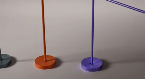 Three lamps stand side by side on a pale surface: grey, orange and violet, all with stems folded upright on disc bases. 