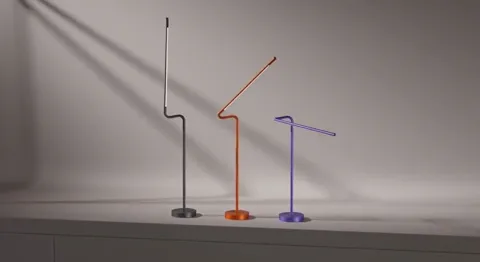 The arms drop lower and the shadows on the wall repeat the bend. The slimness of the stem against the disc base is clear
