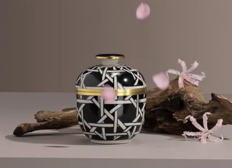 A scented candle in a ceramic jar on a pale surface: a black-and-white geometric pattern, a gold band, a lid in the same