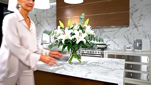She arranges the bouquet, the frame closer. The marble figure becomes visible: large grey veins on white running across 