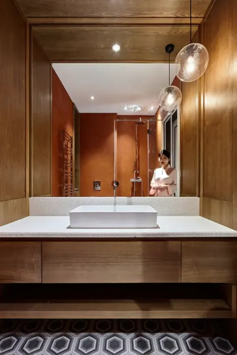A bathroom in walnut panelling: a mirror across the whole wall, a stone counter with a vessel basin, a slim tap, pendant