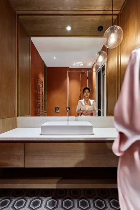 A woman in a silk robe enters from the right and the mirror catches her reflection. Her figure sets the counter height a