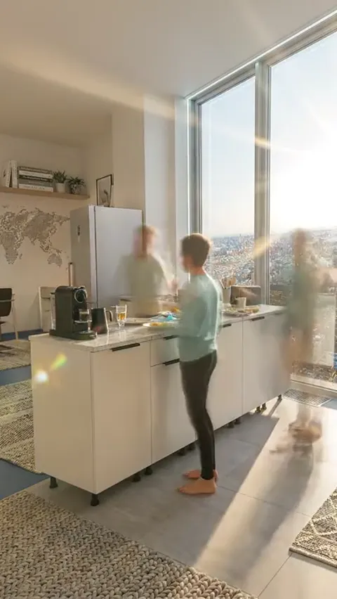 A kitchen in a high-rise apartment, a window onto the city. People at the island are blurred by motion — a time-lapse, w