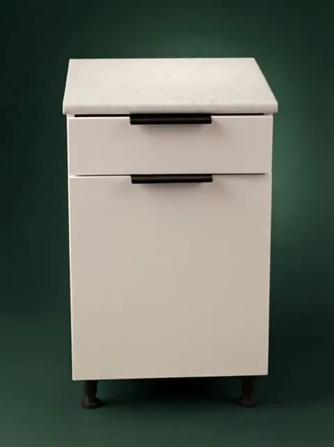 The module closed against dark green: an upper drawer and a lower door, both with black handles, a stone worktop above.