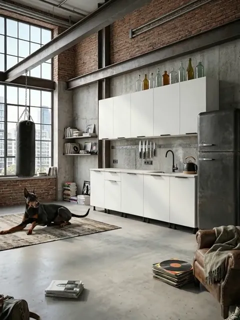 A loft with a brick wall and tall windows: a long run of white kitchen modules along the wall, wall cabinets above, a da