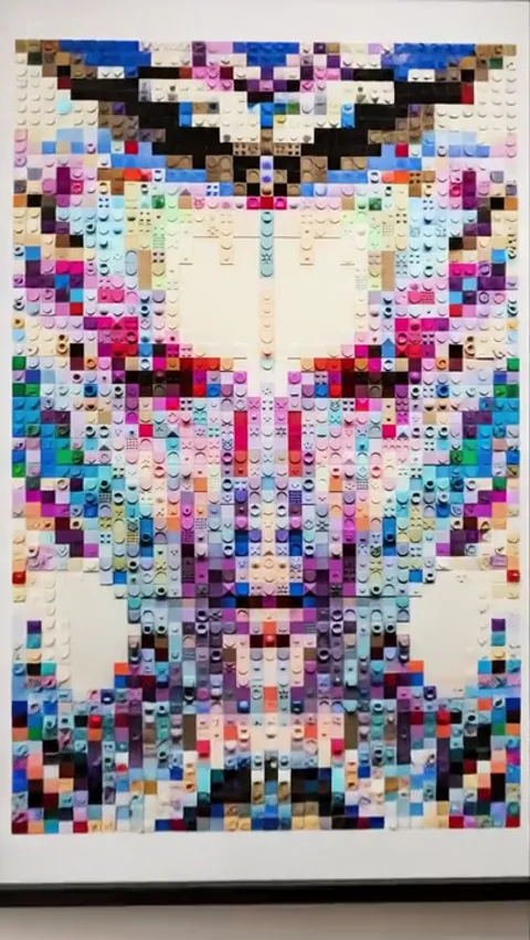The picture close: a woman's face assembled from square elements of different colours, like a mosaic of construction bri