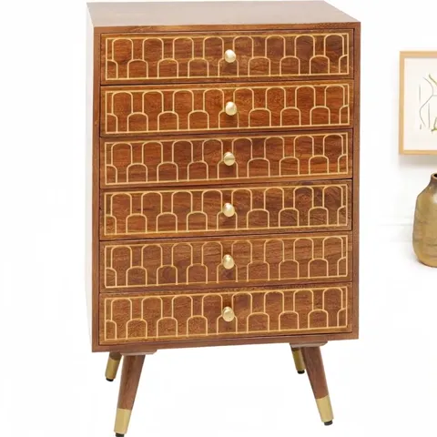 The chest against a pale wall: six drawers, brass inlay in an arched pattern on the fronts, round knobs, tapered legs wi
