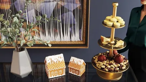 A festive table against a dark blue wall: a three-tier brass stand loaded with macarons, a vase, gingerbread houses and 