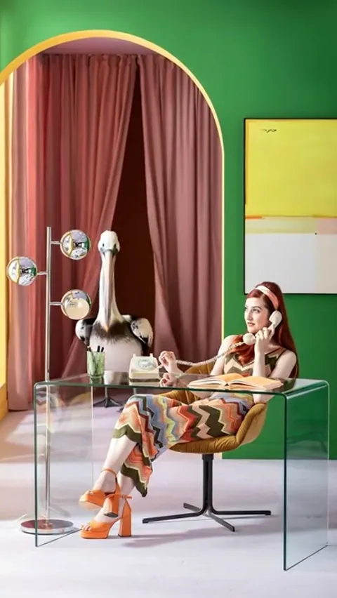 A pelican emerges from behind the curtain. The absurdity enters while the desk stays transparent — the eye has nothing t