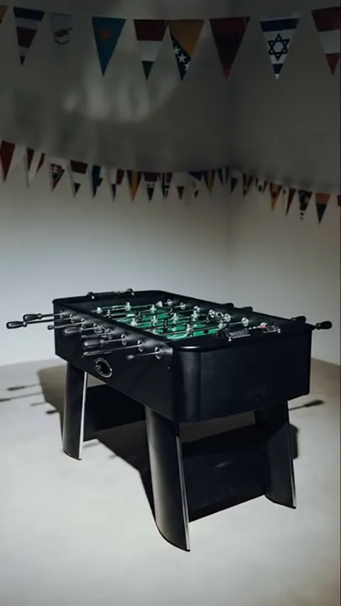 A bright room with bunting: a black foosball table on wide legs, a green pitch, rods projecting from both sides.