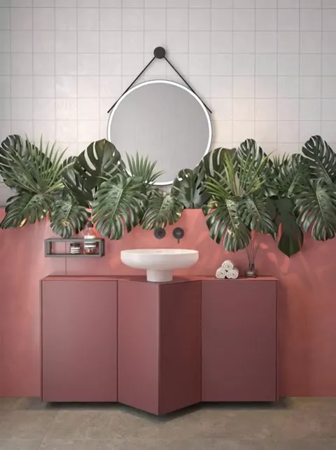 A bathroom with a terracotta vanity and a wall in the same tone, small white tile above, a round mirror on a strap, a ba