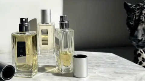 Several bottles of different sizes stand on a marble shelf, a dark ground with lights behind. A jaguar enters from the r