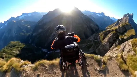 The ridge falls away, the rider against the mountains. The posture reads: torso forward, hands on the bars, feet on the 