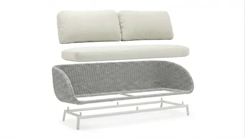 The sofa on white: white cushions on a woven shell, a slim metal frame on legs. The shape reads as a silhouette while th
