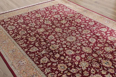 The rug lies at an angle on a wooden floor: a burgundy field woven solid with a fine floral pattern, a wide cream border