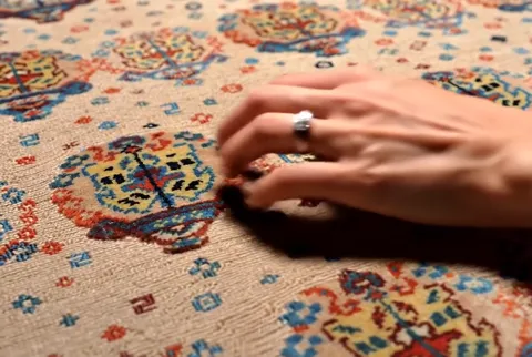 The hand draws across the surface. There is no pile — the palm slides over flat weaving, which makes it immediately clea