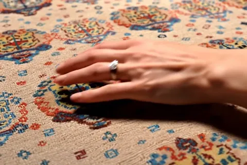 The fingers pass over a medallion. The design is made by the weave itself: the coloured areas lie flush with the ground,