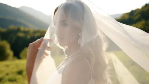 Green hills, a woman in a white dress under a sheer veil. The jewellery is still hidden by the cloth; only silhouette an