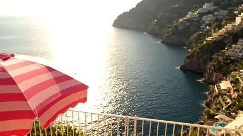 The parasol leaves the frame, opening a view of the bay and a town on the slope. From here it becomes clear exactly wher