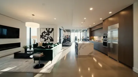 A living room in a new apartment: a green sofa, an island kitchen, floor-to-ceiling glazing. The camera moves forward al