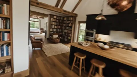 The passage opens onto a library and a kitchen beyond. The rooms connect through an open opening rather than doors — the