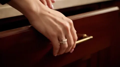 The fingers take the handle, the ring closer to the camera. The setting is visible, and the stone stands proud of the ba