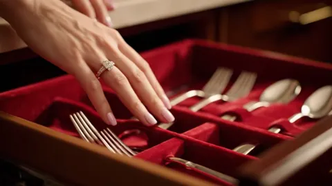The drawer rolls out: red velvet and silver cutlery inside. The red ground behind the hand changes how the stone reads —
