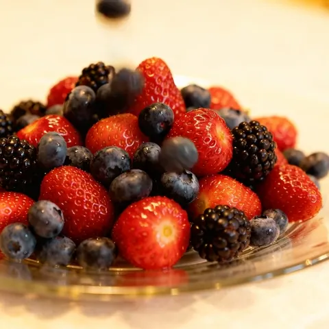 Another berry drops from above. The mound shifts — the fruit is fresh and firm rather than previously frozen.