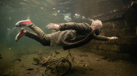 The finale: he glides over the bicycle, sneakers in frame. Six seconds have shown that an underwater shoot with an elder