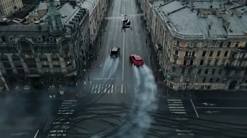 From above: the whole street, the cars fanning out. An aerial at speed — in live production that means a helicopter and 