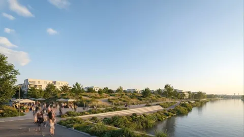 A waterfront with the city beyond: the plot is empty, only greenery and a path. People walk along the river.