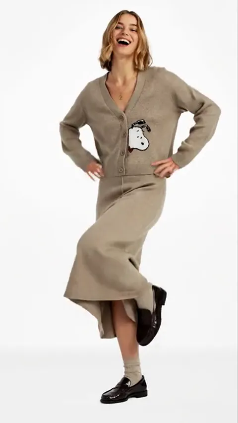 Full length, hands on hips. The length of the cardigan against the skirt is clear: it is cropped, the waistline falling 