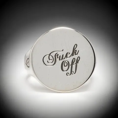 The background turns near-black and the ring is rim-lit. The engraving reads best this way: the letters cast shadow insi