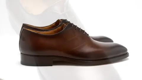 The shoe stands on white in near profile: brown leather with pronounced patina, darker at the toe and lighter toward the