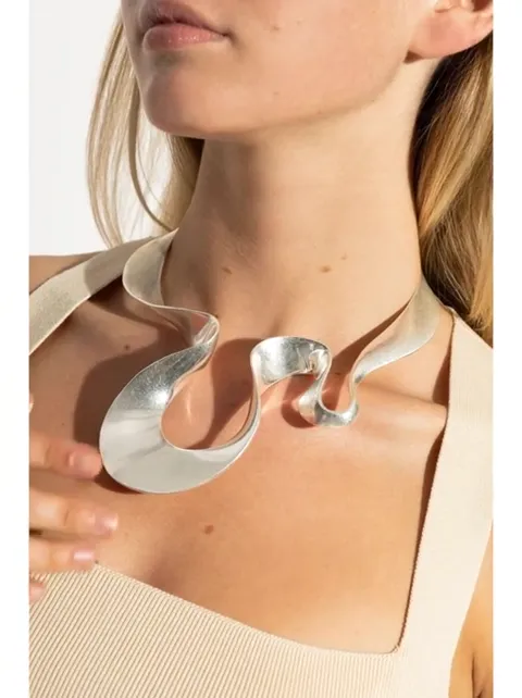 A neck close up: a silver choker of broad wavy ribbon twisted through several bends. The metal is matte, with soft highl