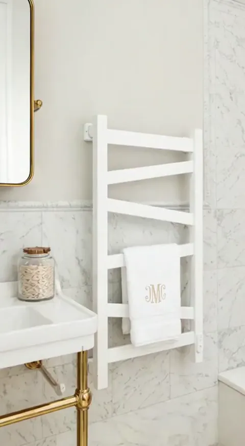 A marble bathroom: a white towel radiator on the wall, a monogrammed towel over the lower rail. The unit is off and the 