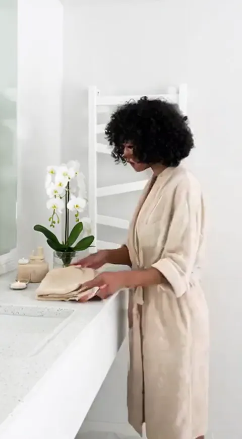 Another bathroom, a woman in a robe folding a towel at the mirror. The radiator behind her is from the same range in a d