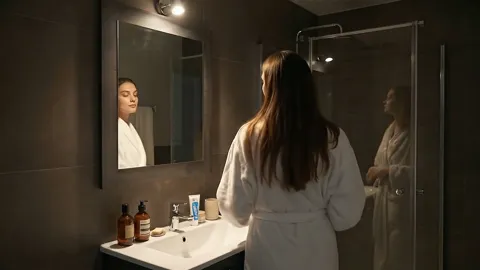 The finale: the woman deep in frame, the set in the foreground. Eight seconds have shown the furniture in a dark bathroo